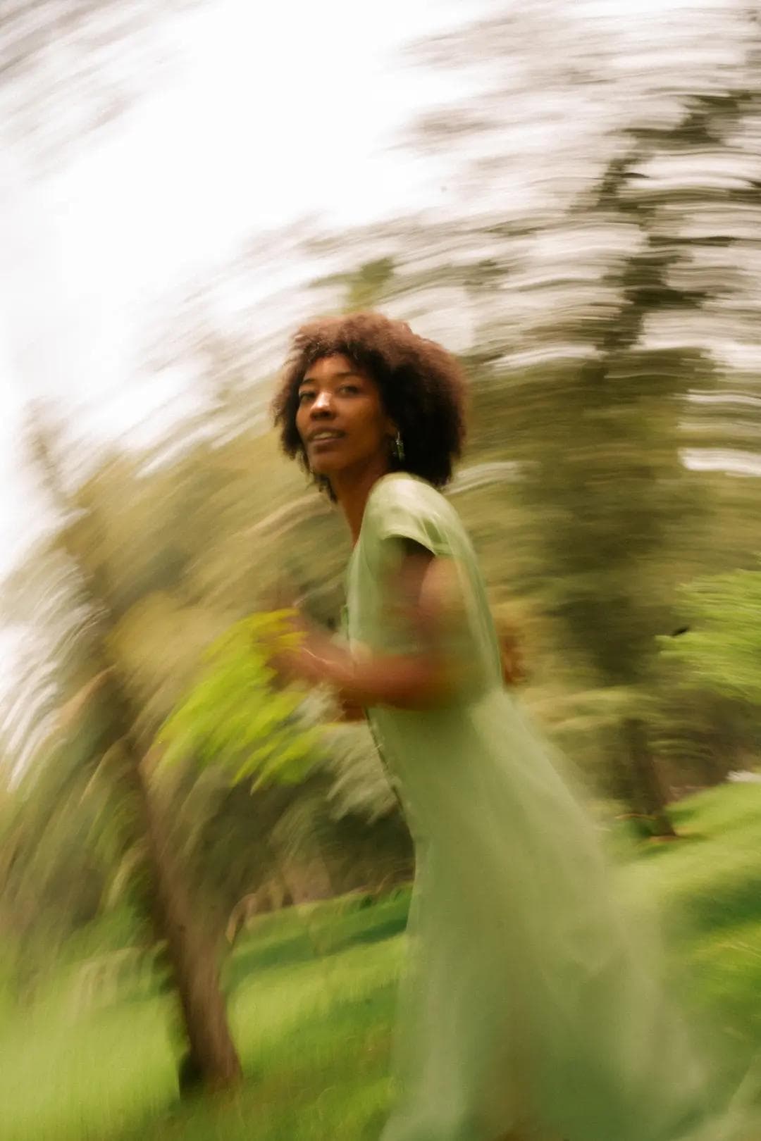 Artistic motion shot of a woman in a flowing green dress running through a lush park, capturing a sense of freedom, natural beauty, and vibrant energy.
